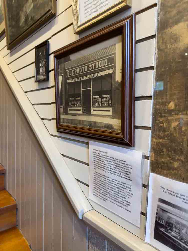 Vintage photo of a building with storefront description, framed artwork, and display information at a cultural or historical exhibit.
