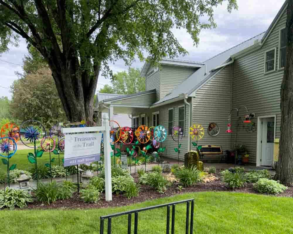 Colorful wind spinners decorating the garden outside a cozy house, creating a vibrant and whimsical atmosphere for outdoor relaxation and enjoyment.