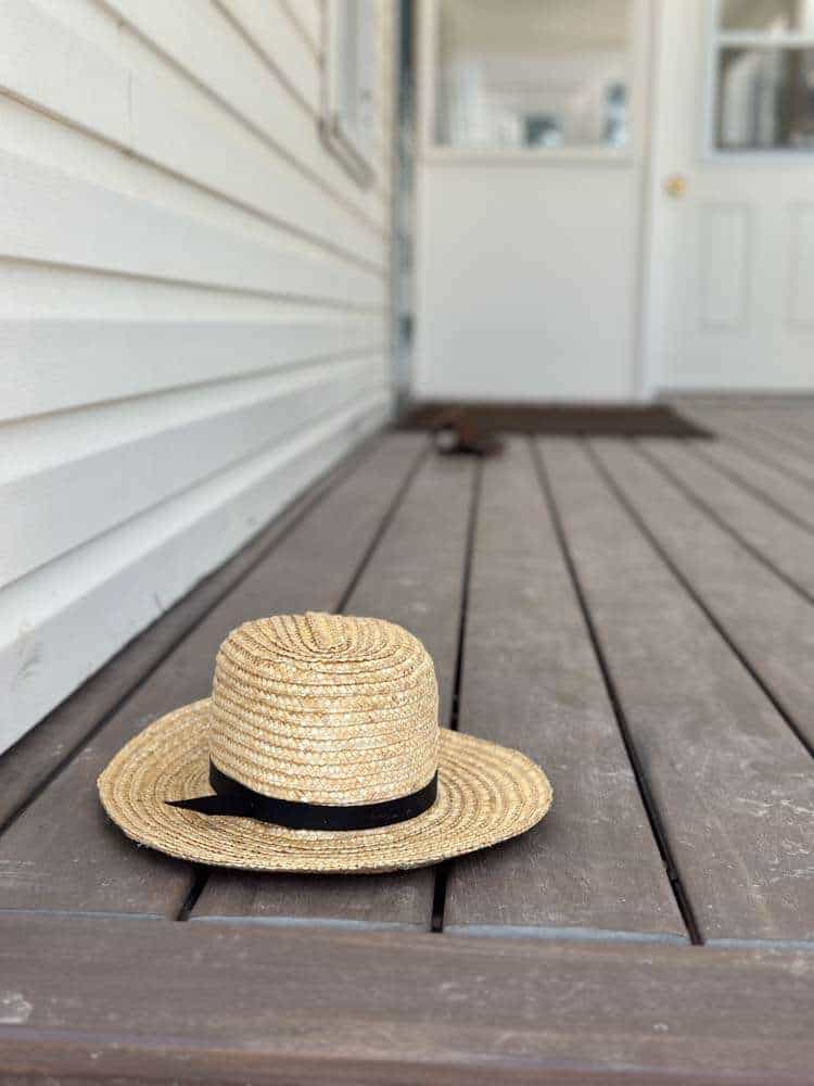 Straw sun hat with black ribbon on wooden porch deck, relaxing summer fashion for grandmas.