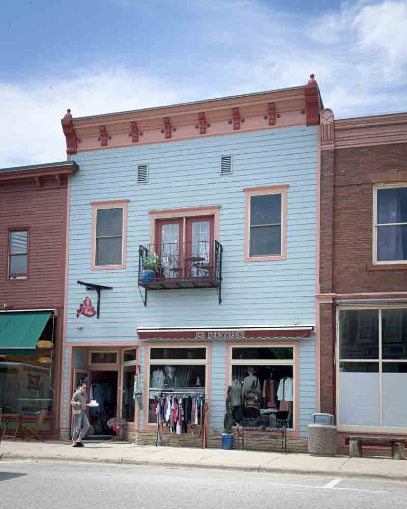 Charming storefront in a small town with vintage architecture and outdoor clothing display, capturing the cozy, nostalgic vibe of a hip grandma life community.