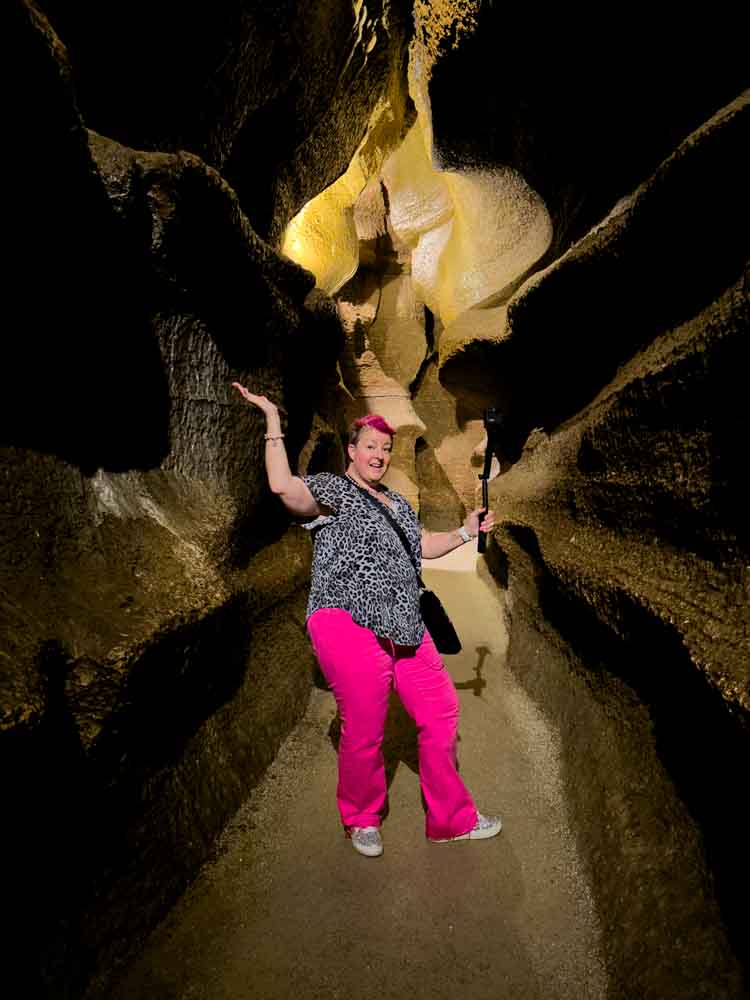 Adventure-loving grandma exploring narrow canyon with flashlight in natural rock formations.