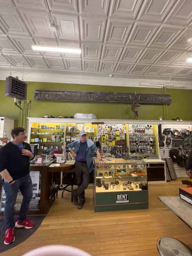 Vintage hardware store with displays of tools and equipment, busy customers browsing and chatting, warm wooden floors, and a vibrant arcade of industrial goods.