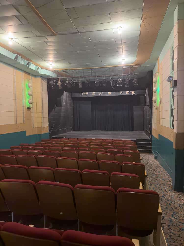 Empty theater stage with red cushioned seats, perfect for live performances or entertainment events, in a cozy venue with vibrant lighting.
