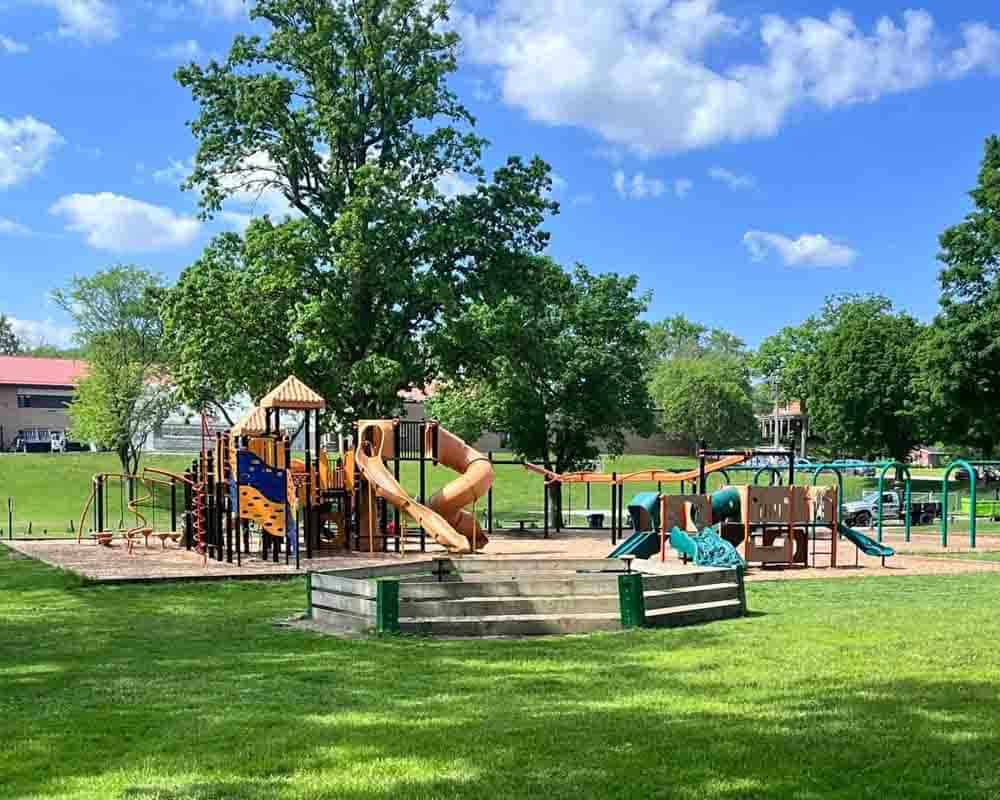 Colorful playground equipment with slides and climbing structures in a sunny park setting, perfect for children and family fun, surrounded by lush green grass and mature trees.