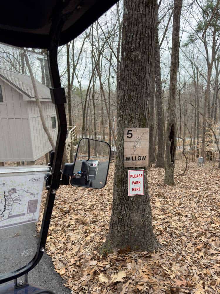 A scenic wooded area with a parking sign on a tree, designated for golf cart parking, surrounded by autumn leaves, featuring a small building, perfect for outdoor activities and nature lovers.