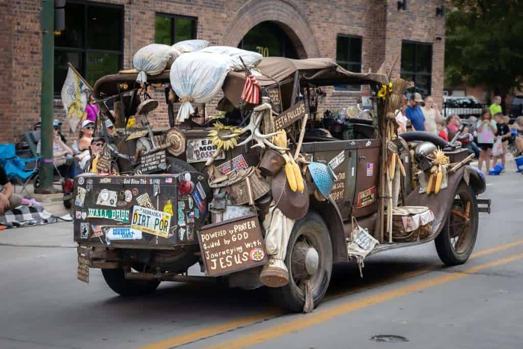 Decorated vintage car in a Fort Dodge, Iowa parade covered in signs, trinkets, flags, and quirky roadside-style ornaments.