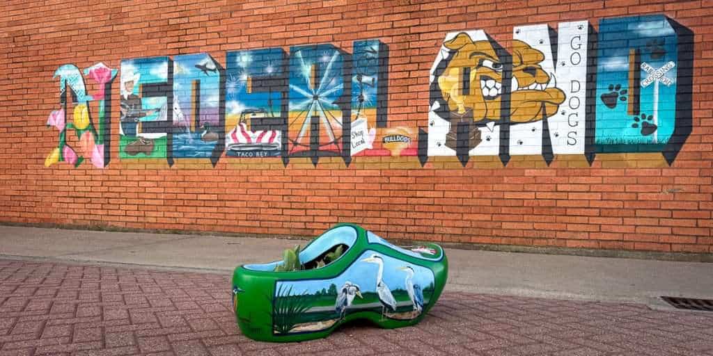 Painted wooden shoe sculpture in front of Nederland Texas mural