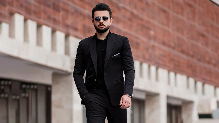 Stylish man in black suit and sunglasses walking outdoors.
