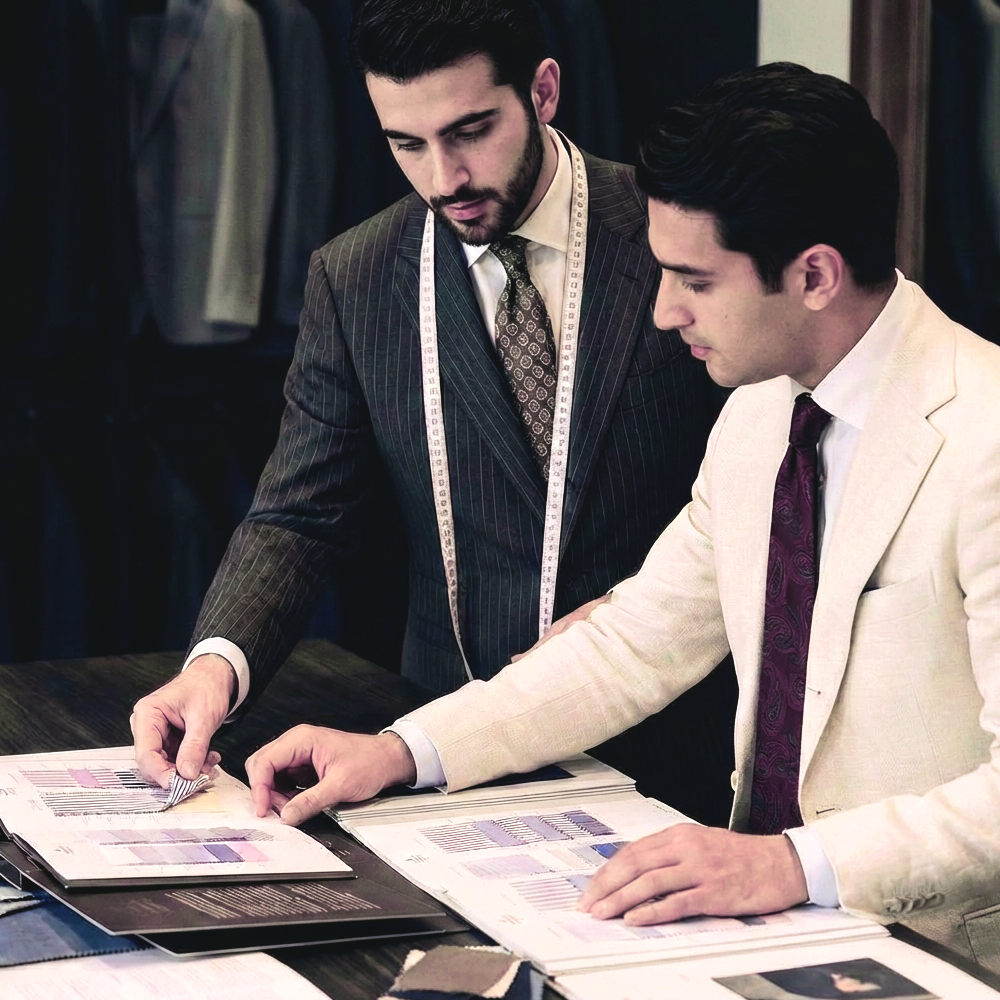 Tailors discussing fabric samples for custom suits at H.M. Cole.