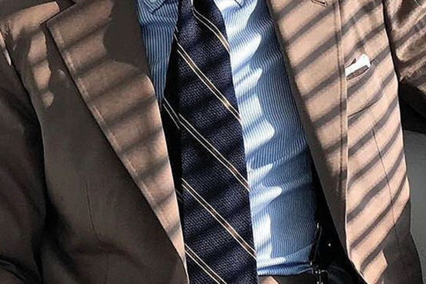 Business professional in a suit with striped tie and light blue shirt, sunlight shadows on the cloth.