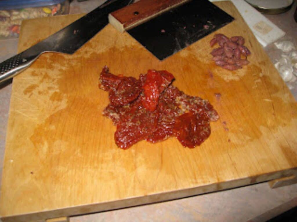 Image shows chopped sundried tomatoes on chopping board.