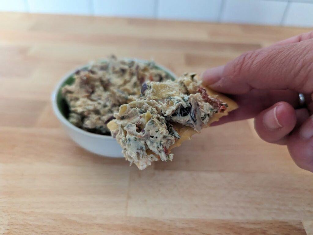 Image shows delicious bite of Tuscan artichoke and sundried tomato dip.