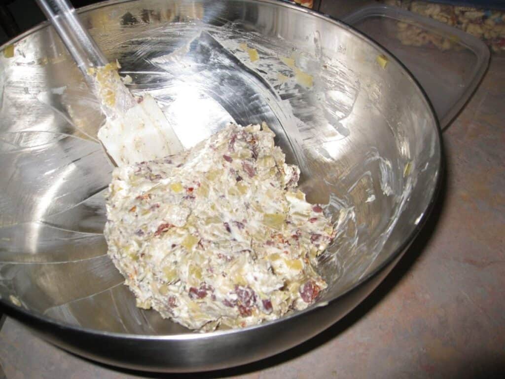Image shows ingredients of Tuscan artichoke and sundried tomato dip mixed together in a bowl.