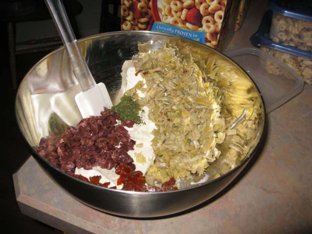 Image shows ingredients of Tuscan artichoke and sundried tomato dip put together in a bowl.