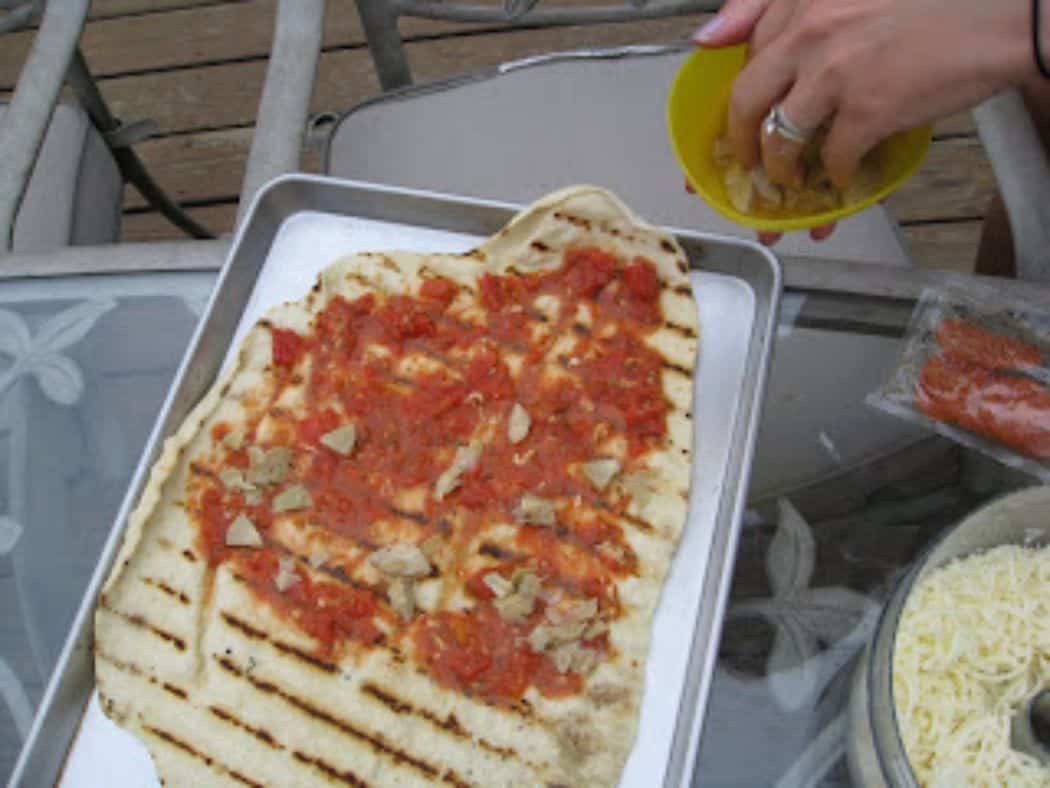 Image shows grilled pizza dough with toppings.