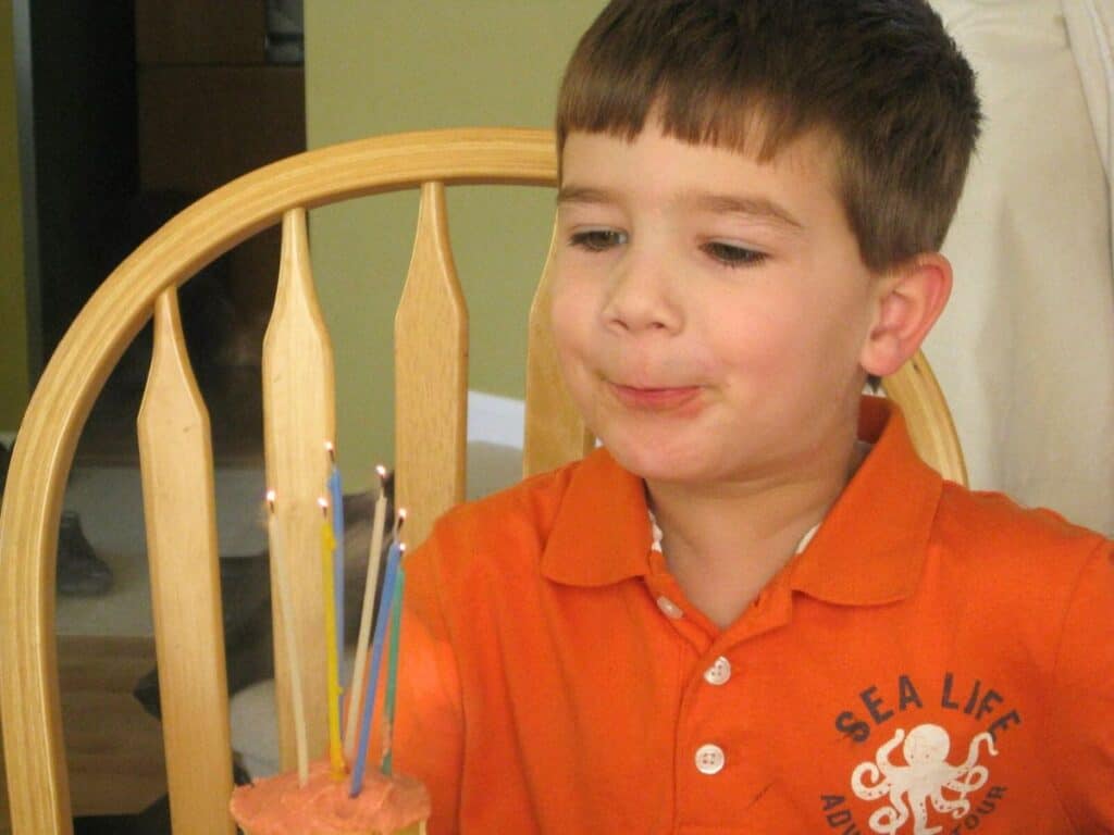 Image shows kid sitting on a chair blowing the lighted birthday candles.