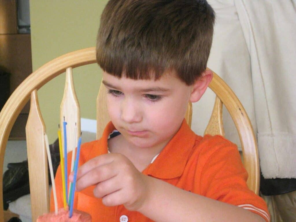 Image shows kid sitting on a chair looking at the birthday candles.