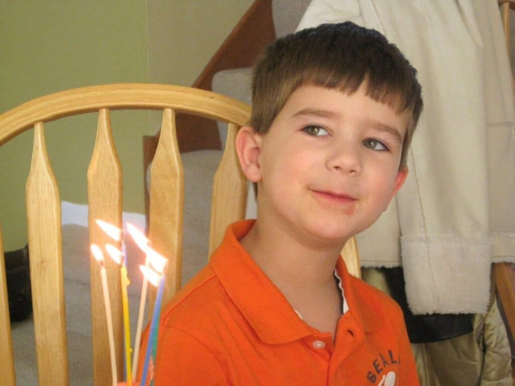 Image shows kid sitting on a chair with lighted birthday candles.