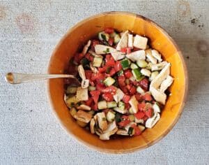 Overhead shot of a wooden bowl of Greek panzanella salad sitting on concrete.