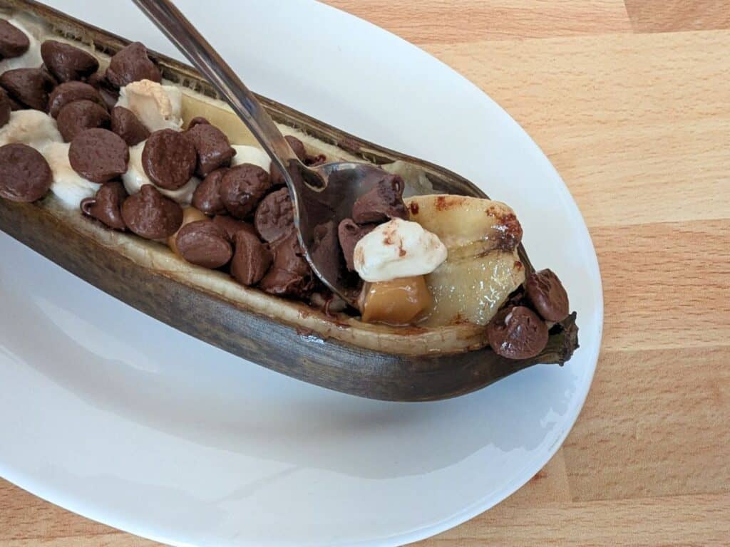 Image shows bite of yummy banana boat on a white plate.