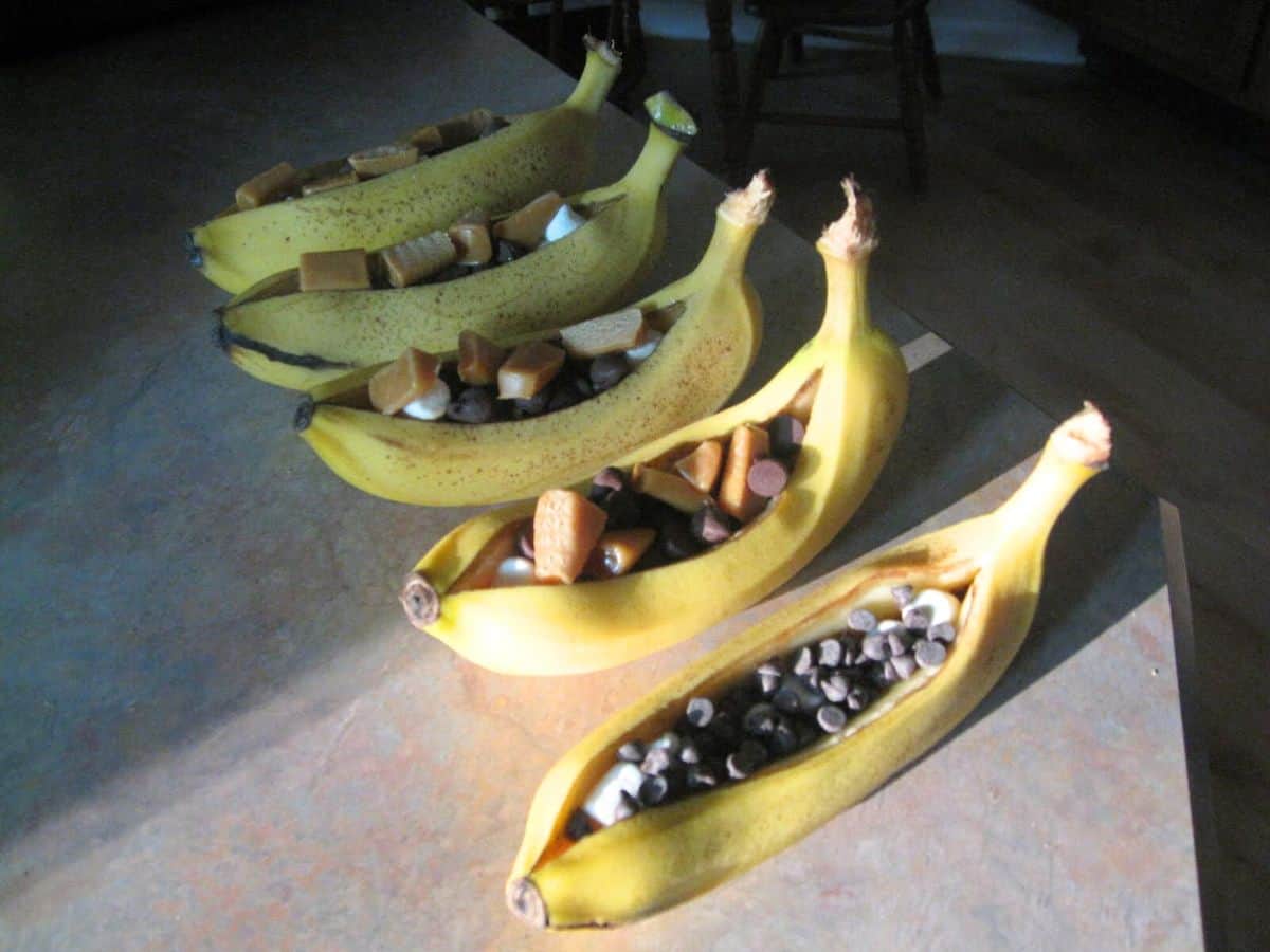 Image shows A ripe banana sliced open and filled with chocolate and caramel and marshmallow, served on a blue plate.