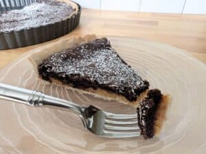 Image shows sliced chocolate and caramel tart on plate.
