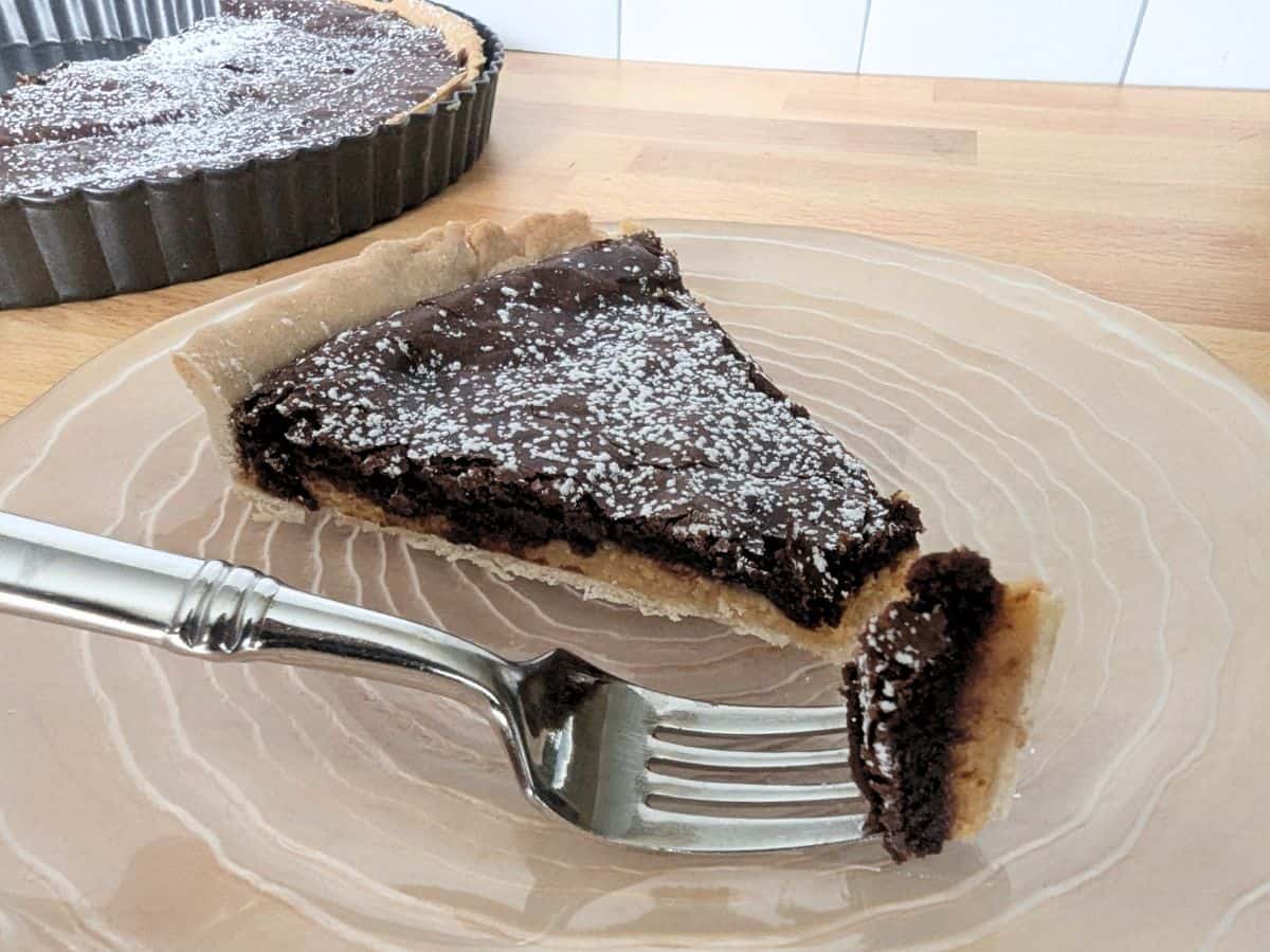 Image shows sliced chocolate and caramel tart on plate.