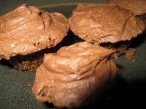 Image shows baked mini chocolate cupcakes with frosting.