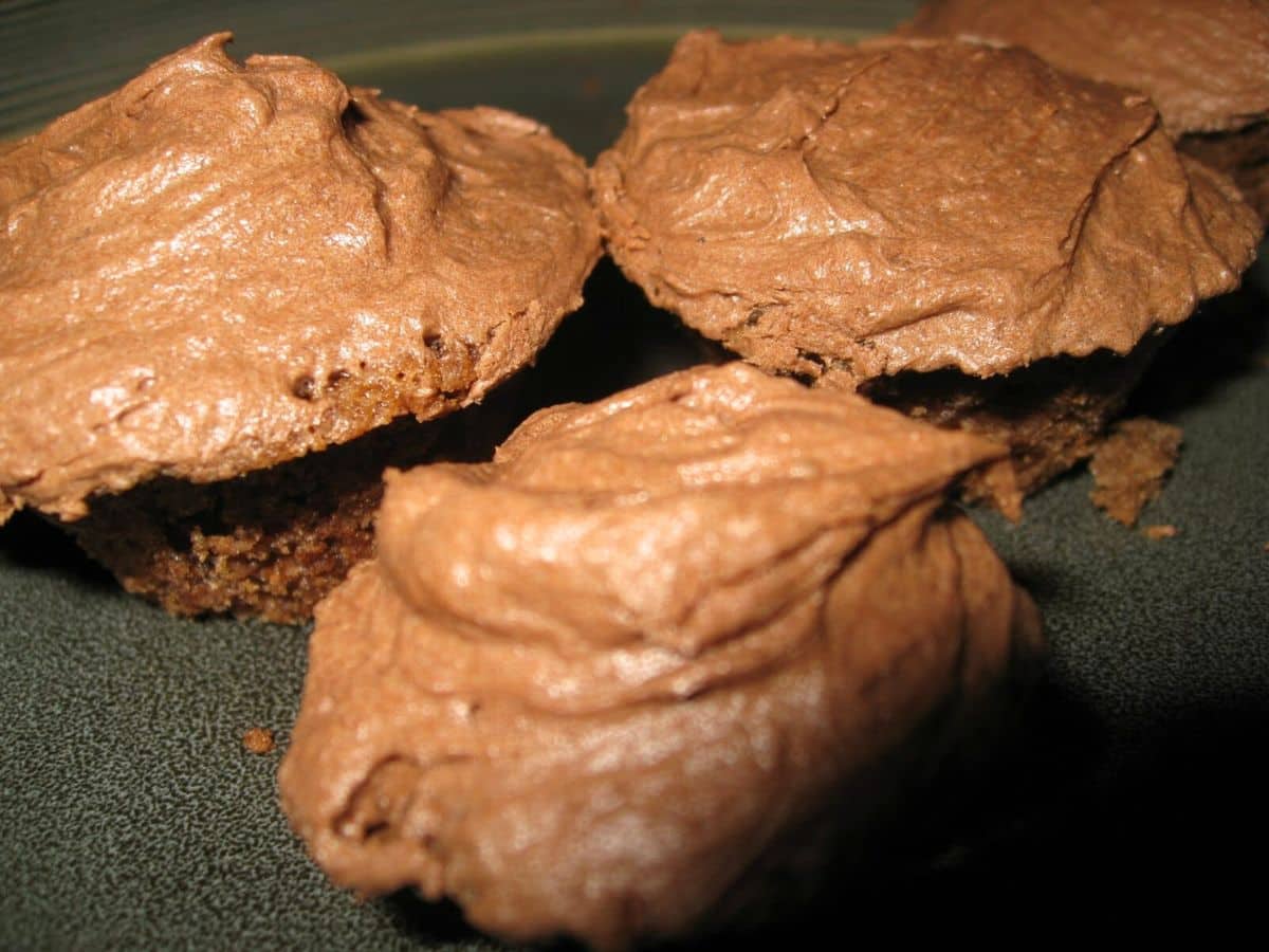 Image shows baked mini chocolate cupcakes with frosting.