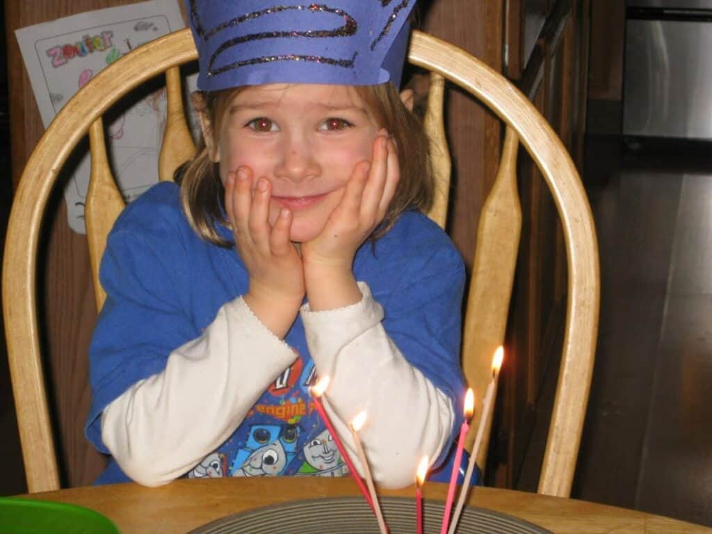 Image shows little girl sitting on a chair with lighted birthday candles.