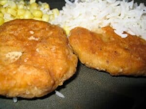 Image shows two salmon patties on a green plate served with rice and corn.