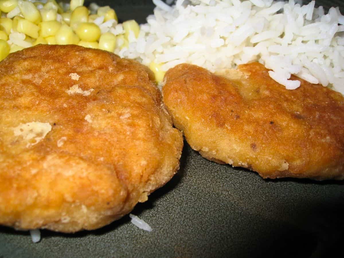 Image shows two Salmon Patties on a green plate with rice and corn.