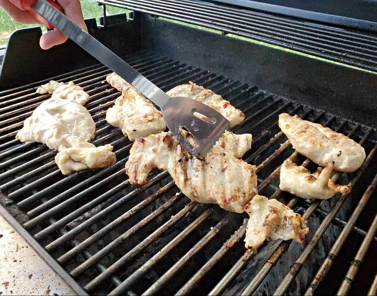 Flipping chicken on the grill with tongs.