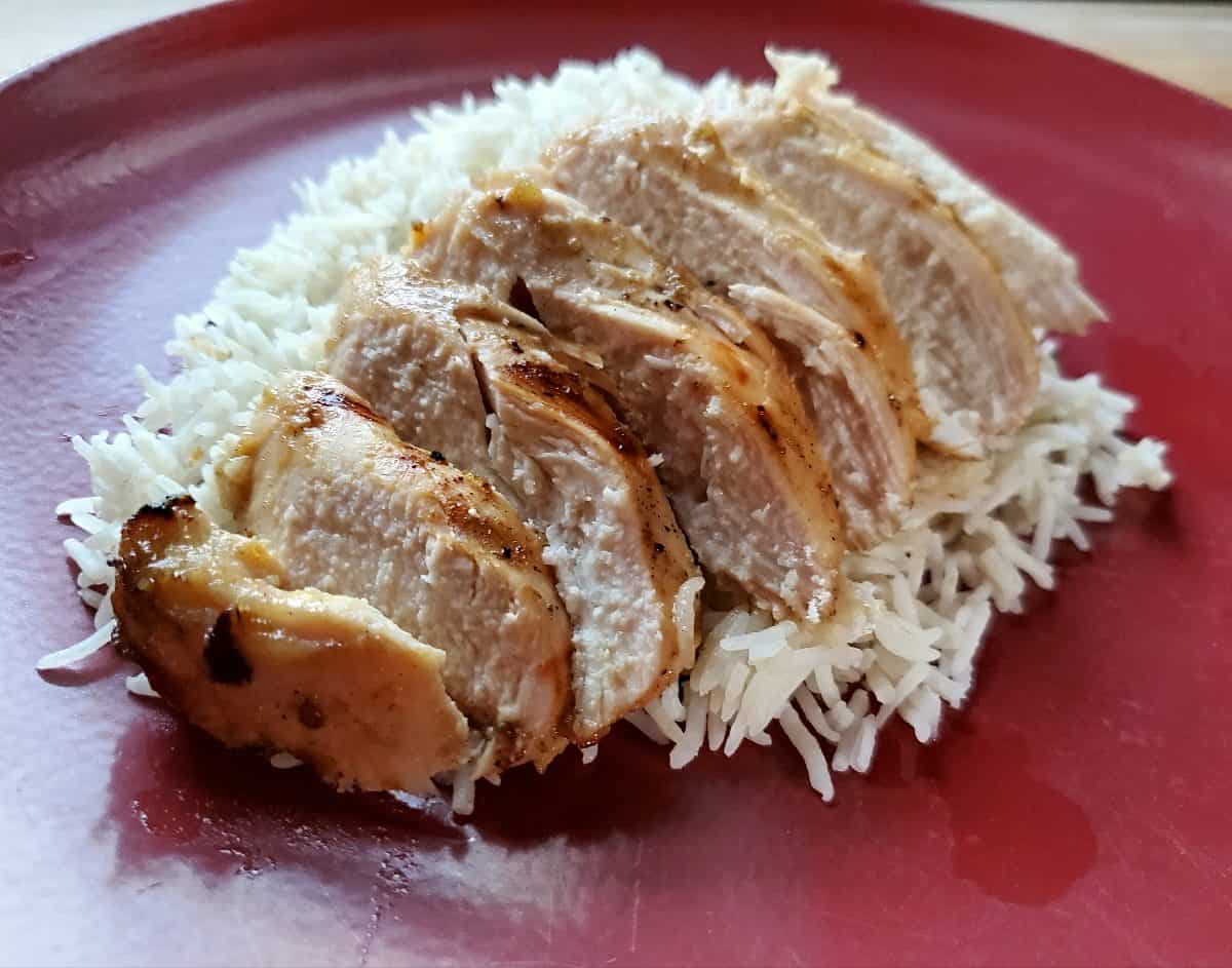 Sliced grilled chicken on a red plate with rice.
