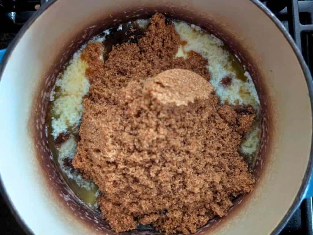 A mound of brown sugar sits on top of melted butter in a saucepan on a stovetop, ready to be mixed for delicious lacy cookies.