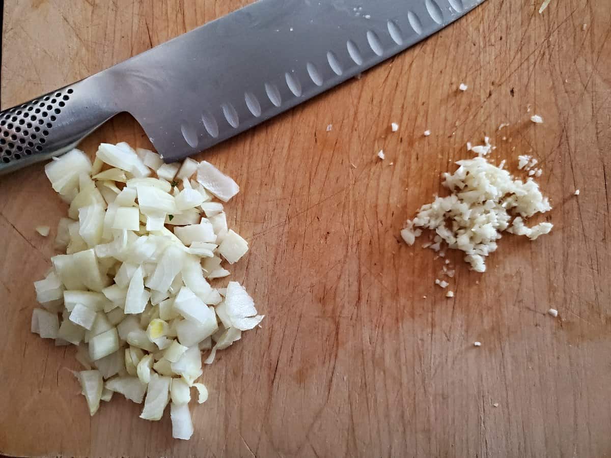 Chopped onion and garlic in piles on a cutting board.