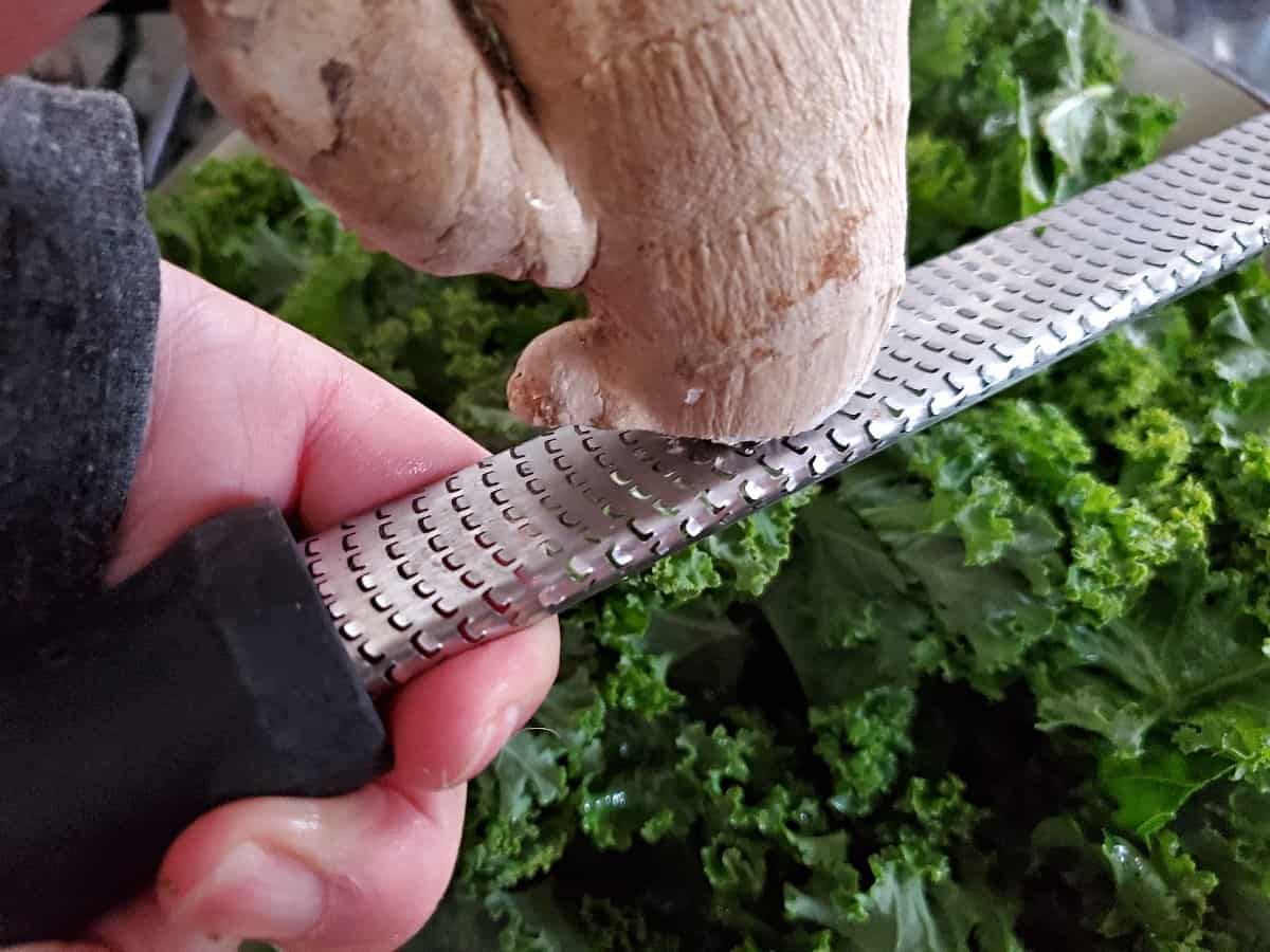 Grating ginger with a microplane zester into kale.