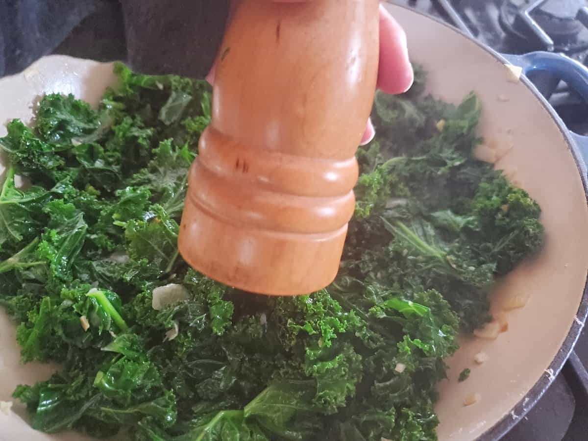 Grating pepper into cooked garlic Asian kale.