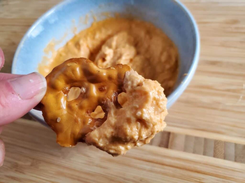 Image shows half of the pretzel dip into buffalo chicken dip in a bowl.