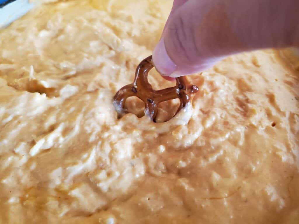 Image shows pretzel dip into the pot with buffalo chicken dip.