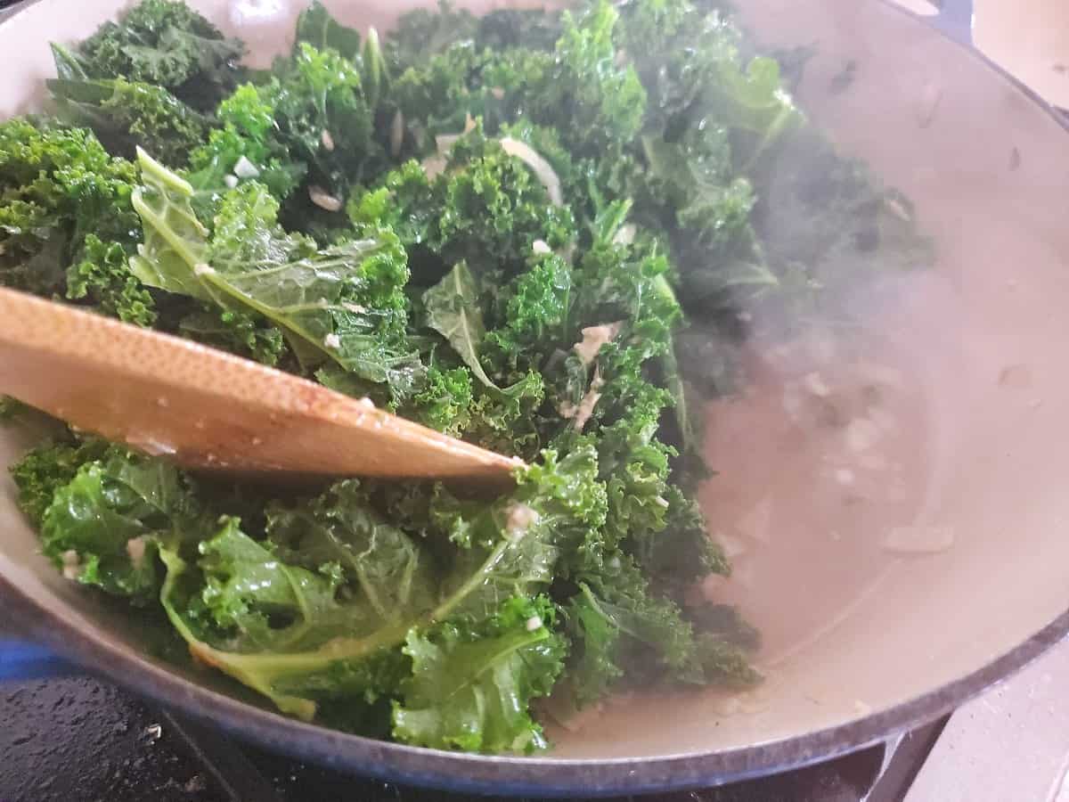 Wooden spoon stirring Asian kale as it shrinks.