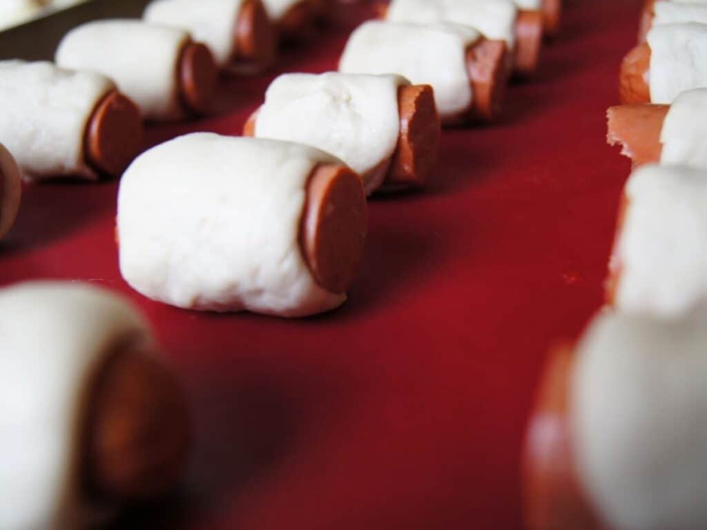 Image shows dough wrapped around hot dogs.