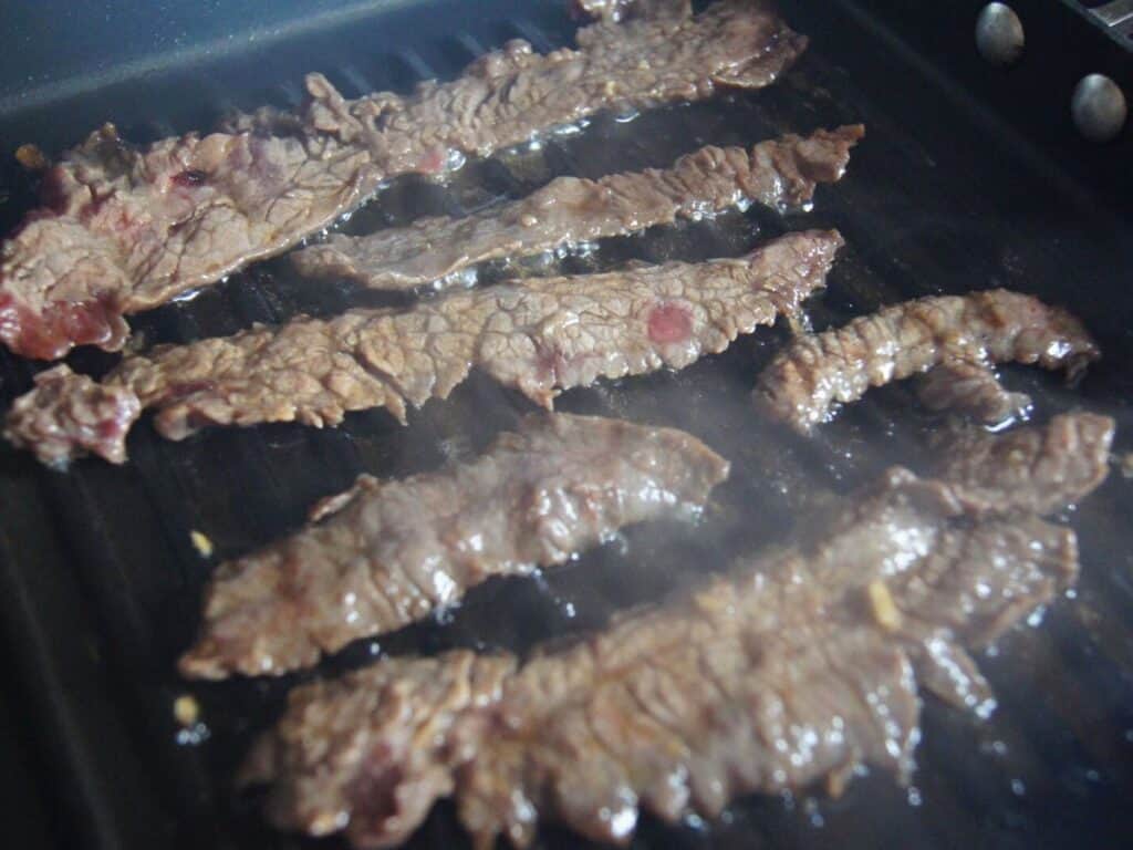 Image shows marinated beef on the grill.