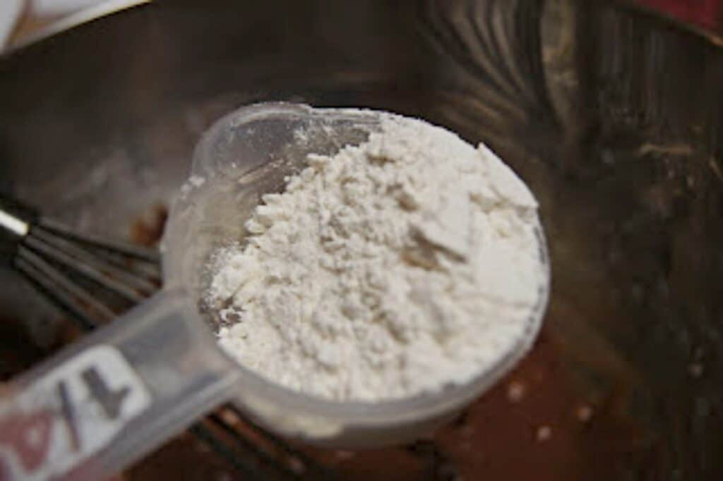 Scant quarter cup of flour held over a bowl of chocolate batter.