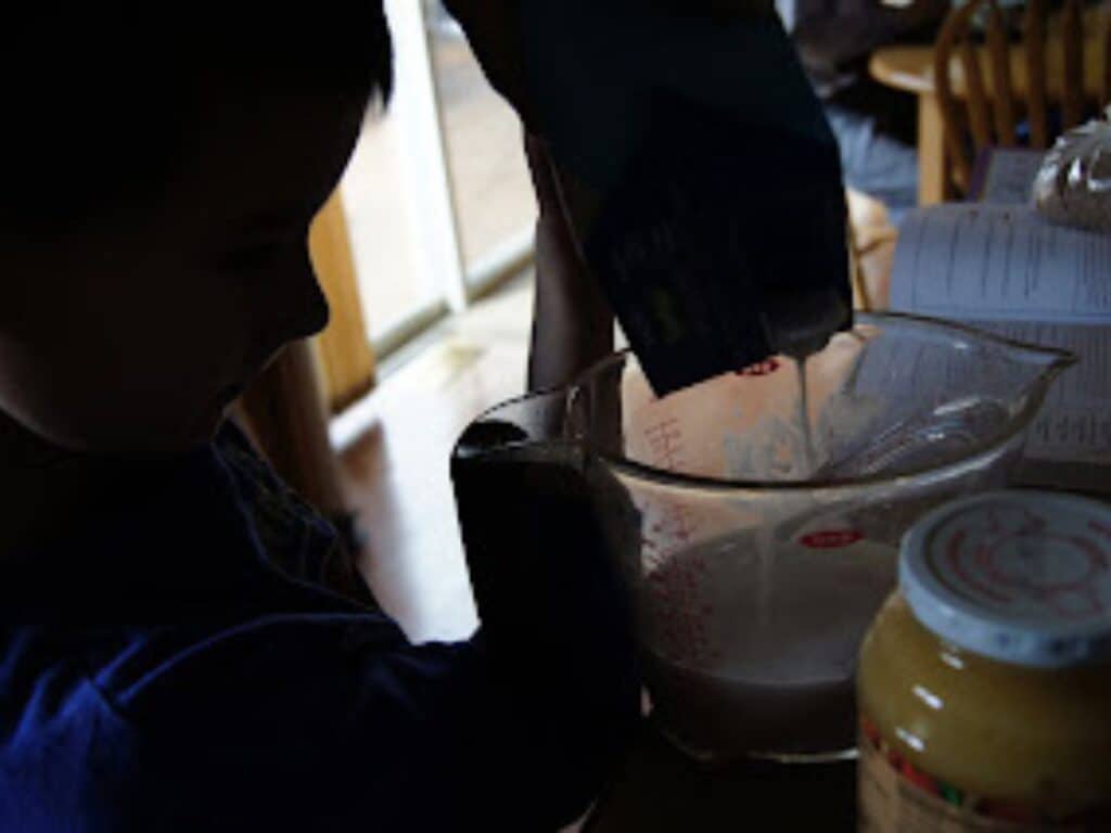 Image shows kid pouring mixture on a large measuring cup.