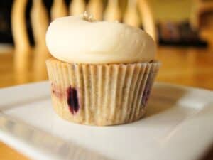 Image shows cherry cupcakes with vanilla frosting on a plate.