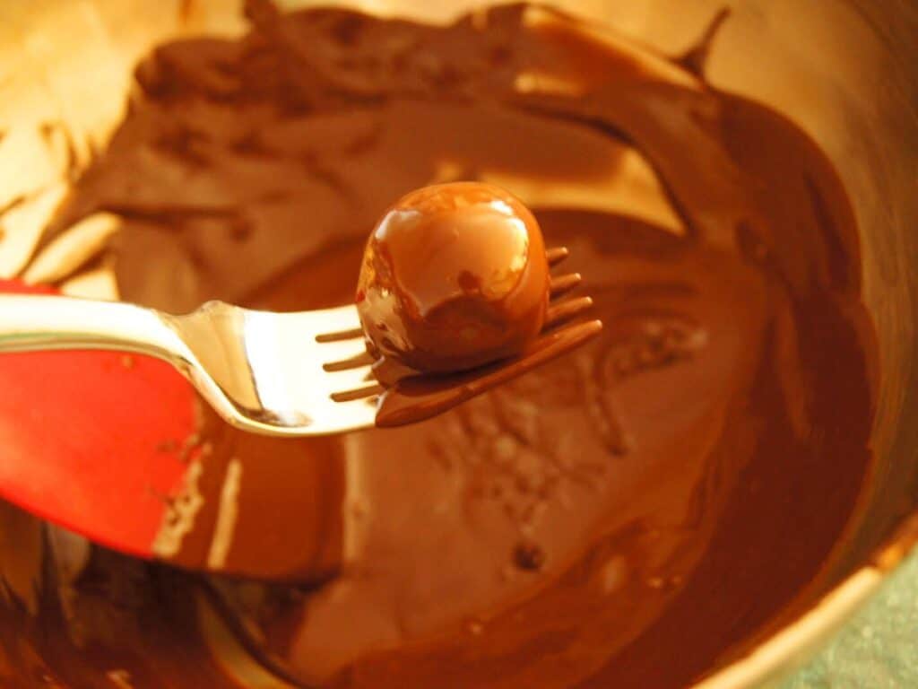 Image shows truffle coated with melted chocolate on a fork.