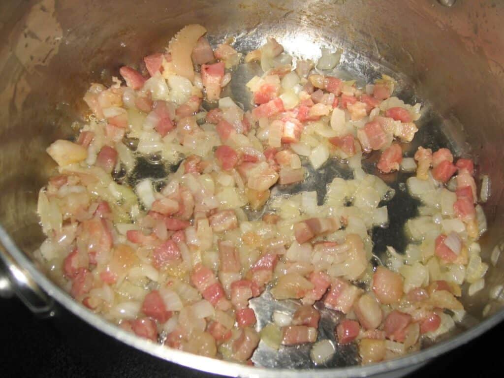Image shows pancetta and onion in a pan.
