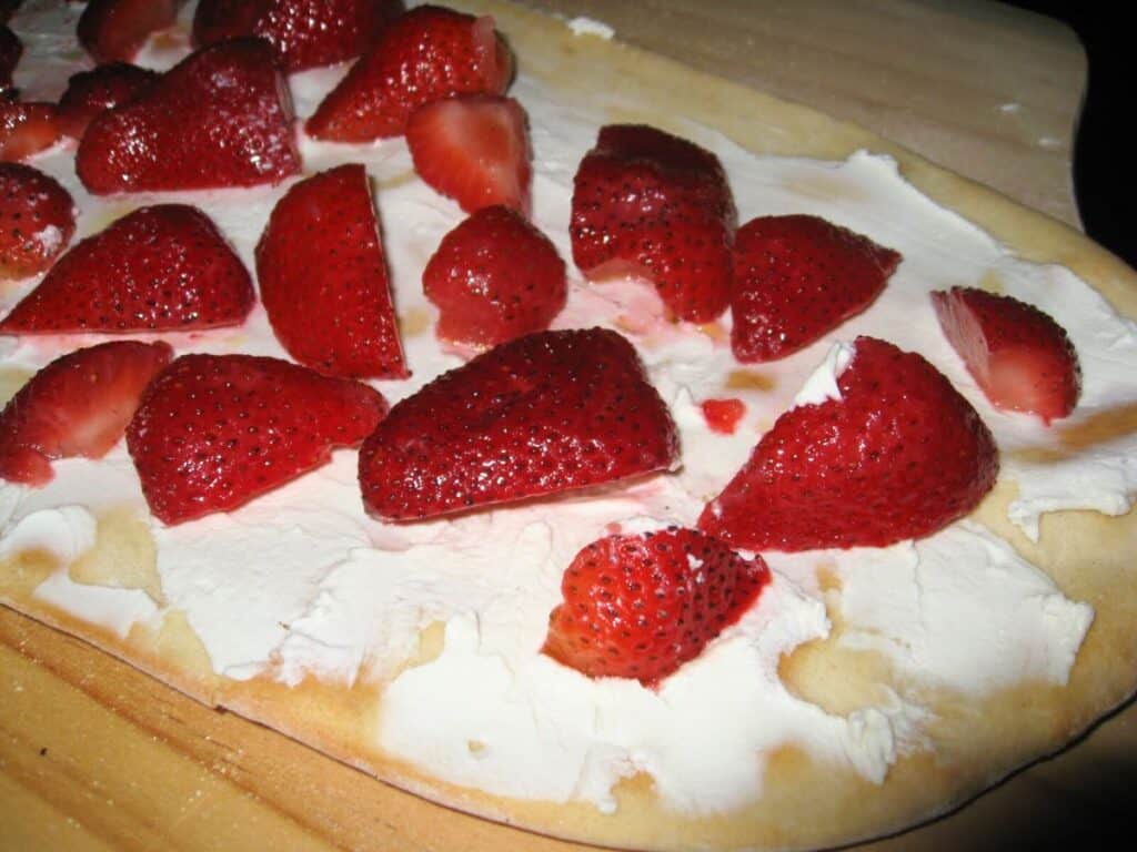 Image shows strawberries on top of goat cheese pizza crust,