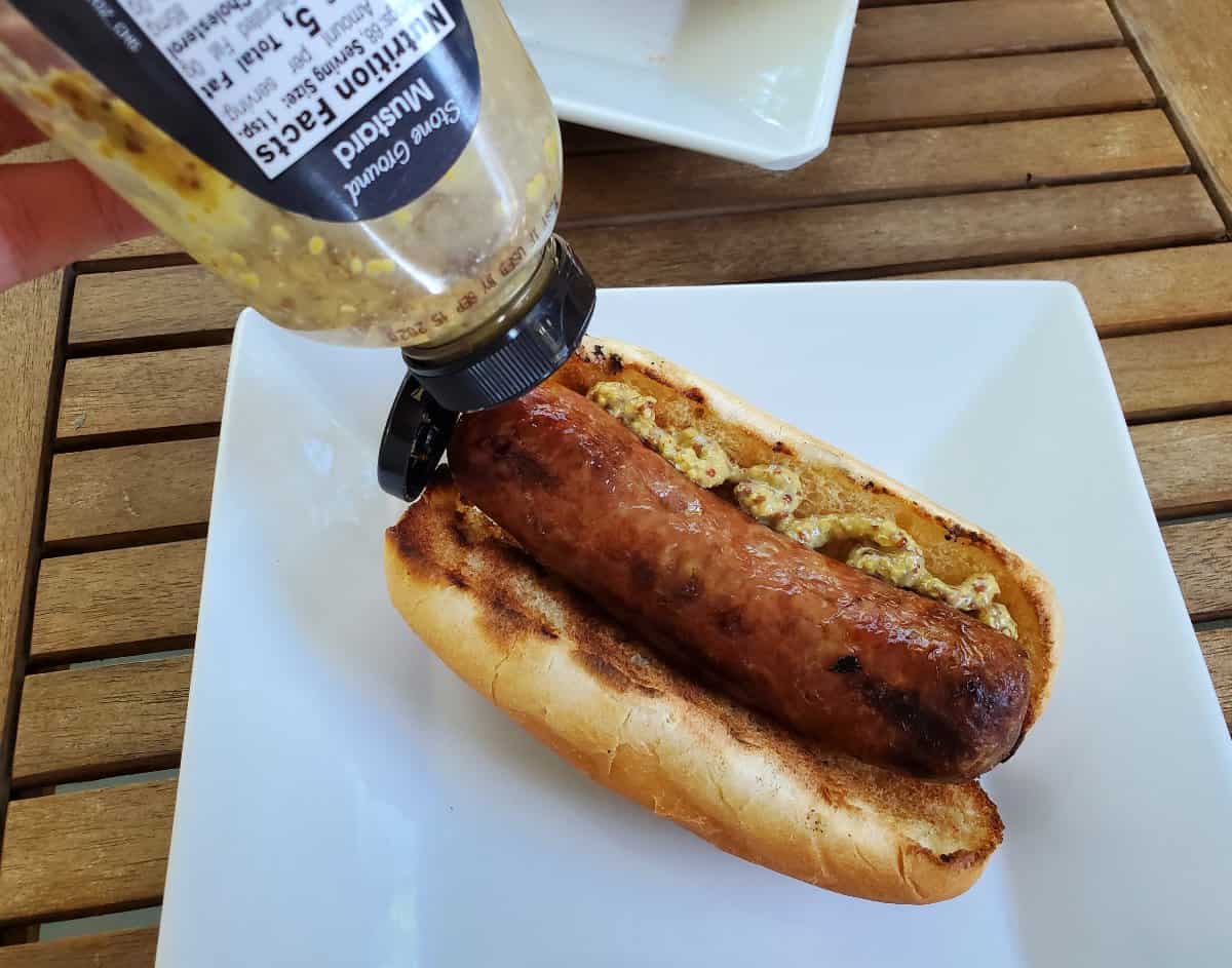 Adding mustard to grilled bratwurst on a bun